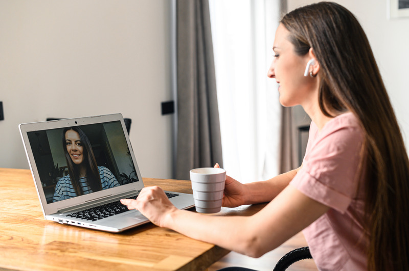 Distance communication with friends via video call, zoom. A young attractive woman talking via video with her friend, she looks at webcamerra with smile. Side view